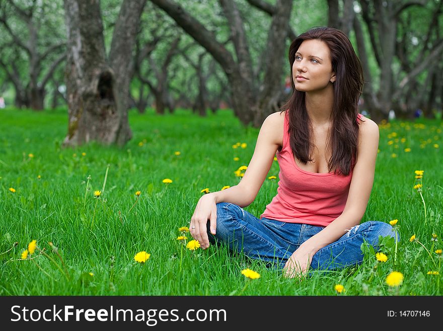 Beautiful brunette girl sitting on grass in jeans