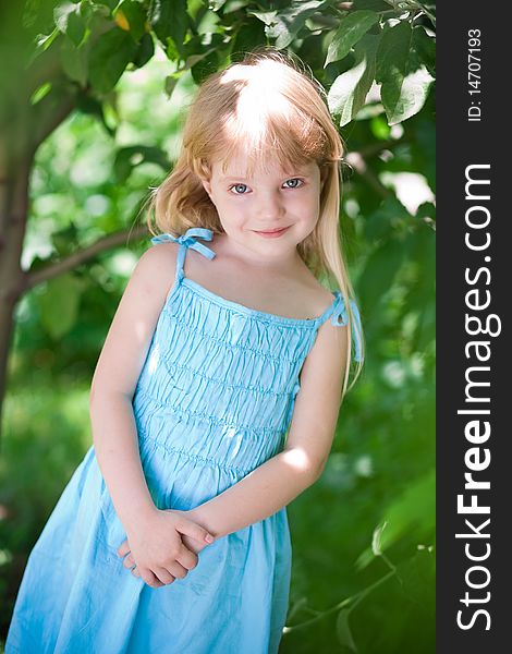 Little girl wearing blue dress in the park under trees