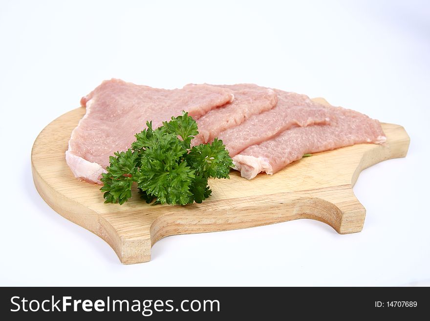 Raw tenderized pork chops on a pig shaped chopping board decorated with parsley on white background