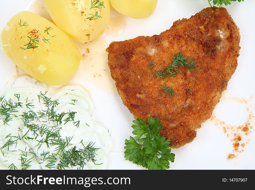 Pork chop (covered in batter and breadcrumbs), potatoes and cucumber salad decorated with dill and parsley on a plate on white background. Pork chop (covered in batter and breadcrumbs), potatoes and cucumber salad decorated with dill and parsley on a plate on white background