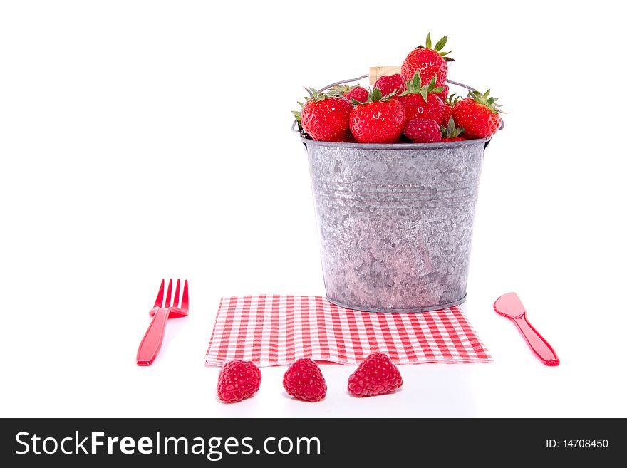 Cutlery with a bucket full of red fruit and a napkin isolated over white