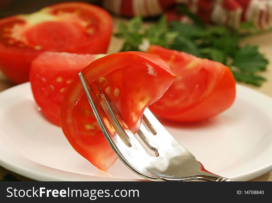 Tomato wedge on salad fork with tomaotes and herbs in background. Tomato wedge on salad fork with tomaotes and herbs in background.