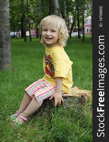 The little girl is sitting on a stump in the grass. The little girl is sitting on a stump in the grass