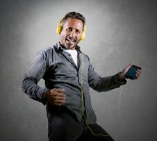 40s Happy And Excited Attractive Man Listening Online Music  With Headphones And Mobile Phone Singing Song And Dancing Carefree Stock Photo