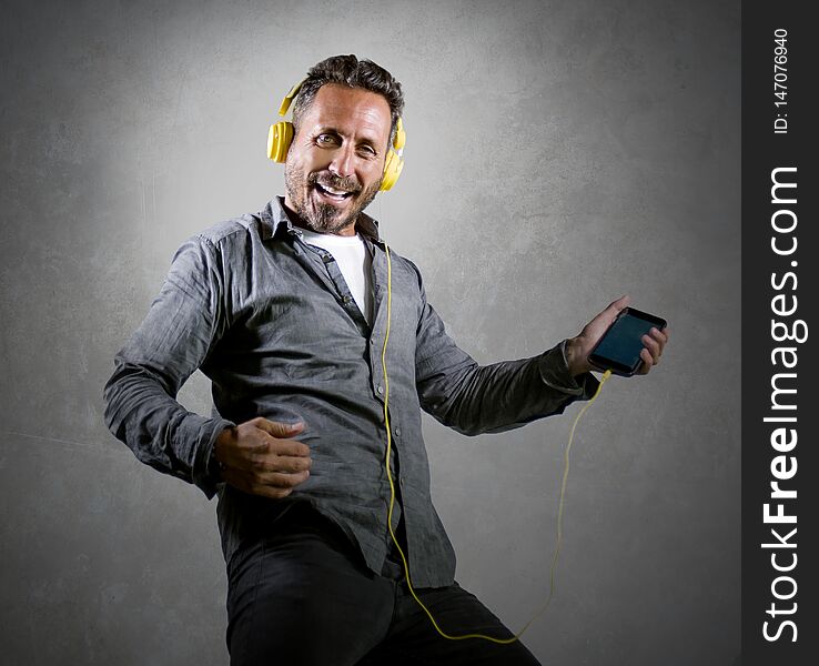 Natural portrait of 40s happy and excited attractive man listening online music  with headphones and mobile phone singing song and dancing carefree isolated on grunge studio background