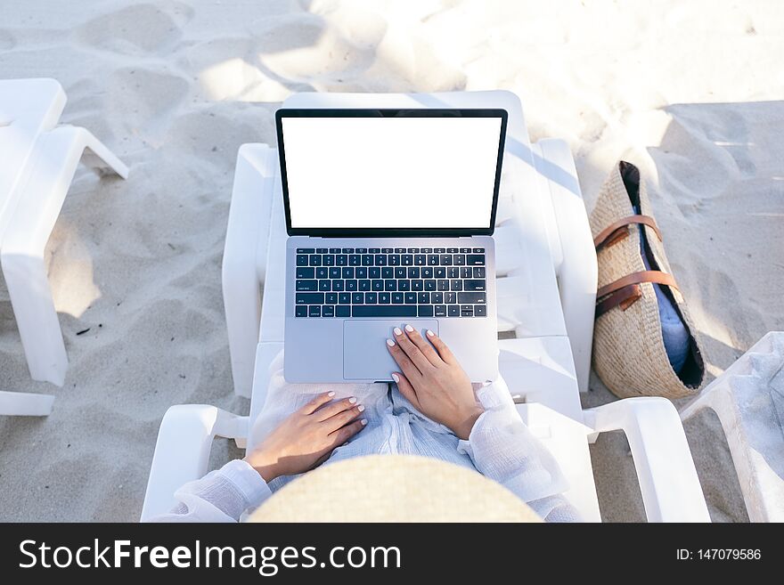 Top view mockup image of a woman using and touching on laptop computer touchpad with blank desktop screen while laying down on beach chair on the beach