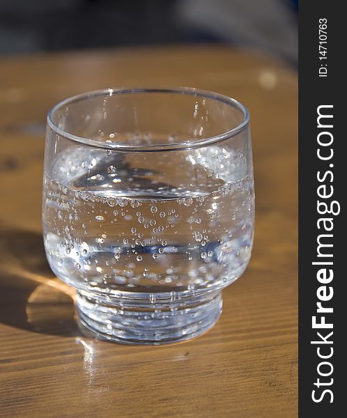 Close-up of a glass of sparkling mineral water on a wooden table in natural light. Close-up of a glass of sparkling mineral water on a wooden table in natural light.