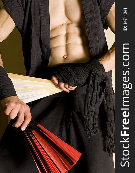The cut mid section of a martial artists body holding combat fans against a wooden background. The cut mid section of a martial artists body holding combat fans against a wooden background.