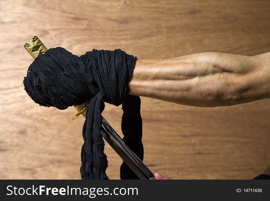 The forearm of a martial artist or samurai holding a japanese katana against a wooden backdrop. The forearm of a martial artist or samurai holding a japanese katana against a wooden backdrop.