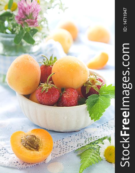 Fresh apricots and strawberries in and beside bowl