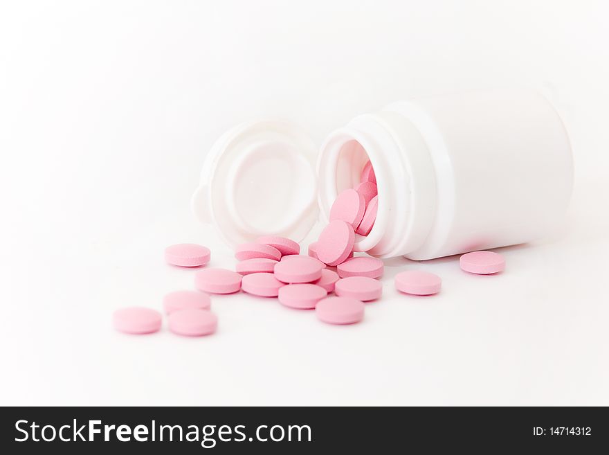 Pink tablets spilled from white vial. Pink tablets spilled from white vial