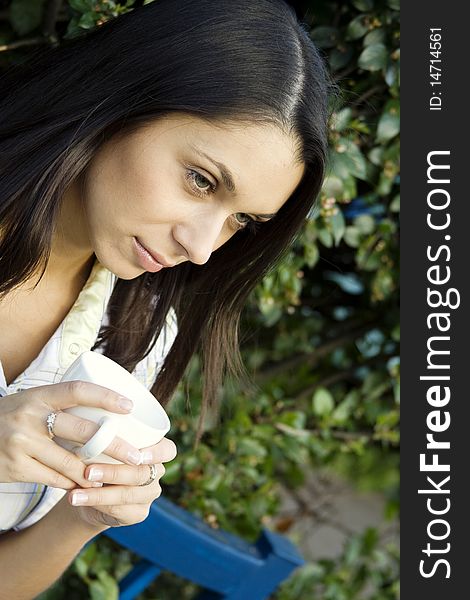 Teen girl resting in a park sitting on a bench in the hands of a white cup with coffee. Teen girl resting in a park sitting on a bench in the hands of a white cup with coffee