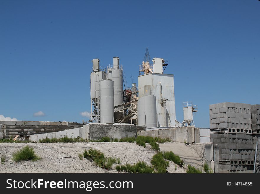 Cement factory against blue sky. Blocks stacked in foreground.