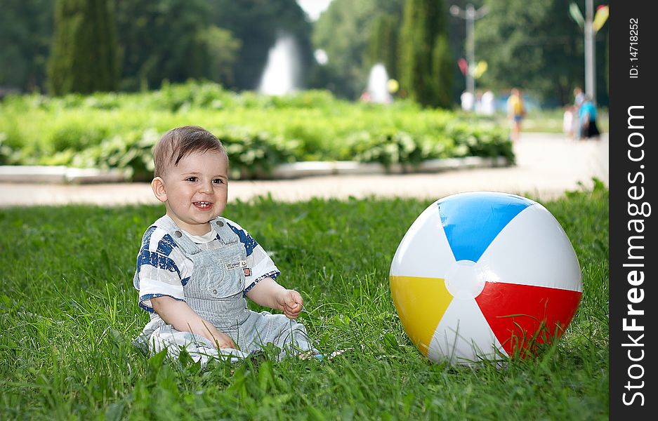 Little boy sitting on grass in the city park, beside the boy is colored ball. Little boy sitting on grass in the city park, beside the boy is colored ball