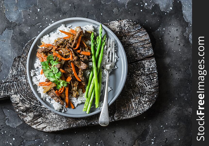 Asian style lunch - spicy fried beef, rice, asparagus on dark background, top view