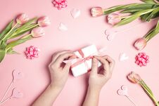 Women`s Hands Decorate Gift Box Surrounded Tulip Flowers And Hearts On Pink Pastel Background Stock Photo
