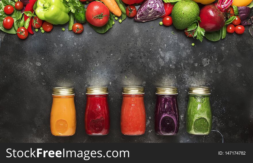 Food and drink background. Colorful vegan vegetable juices and smoothies set in bottles on gray kitchen table, copy space, selective focus