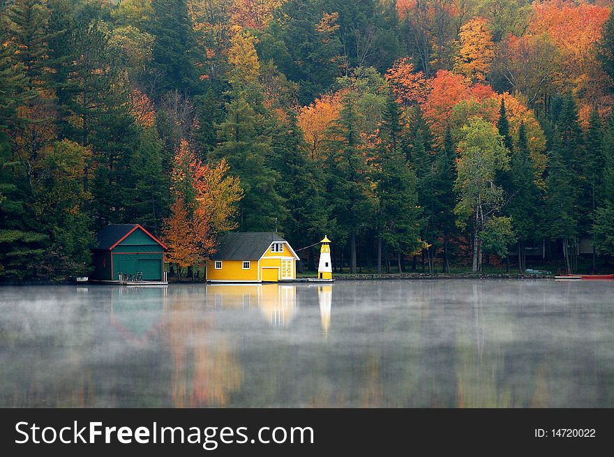 Yellow boathouse appears on early morning misty autumn lake