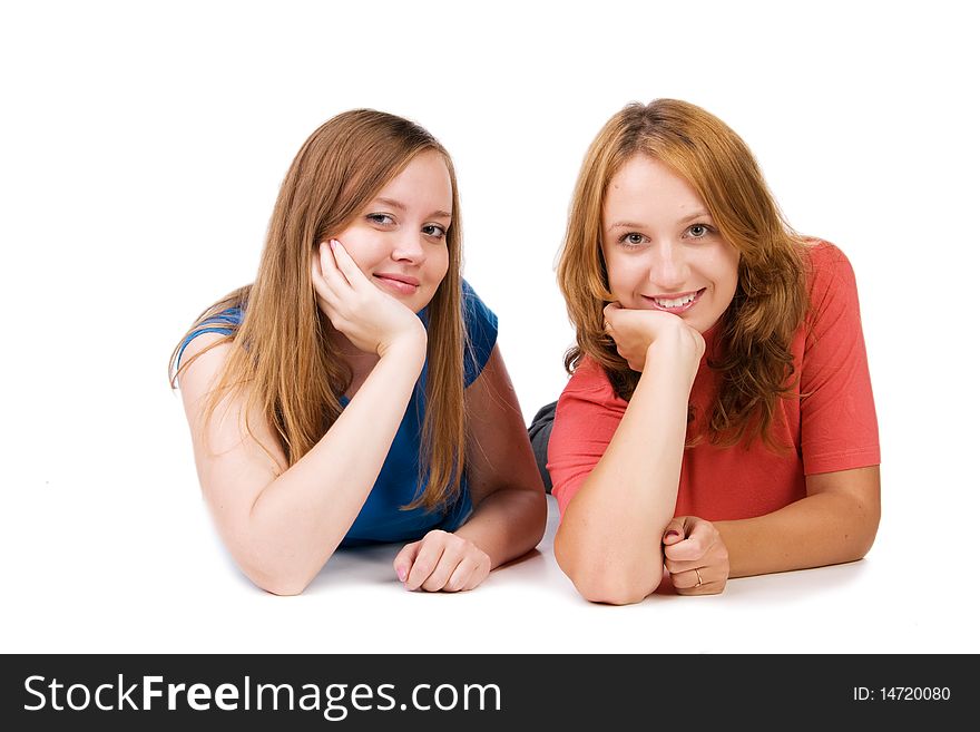 Two beautiful smiling girls lie on a floor, isolated on white