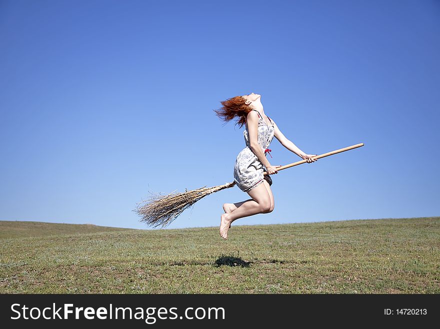 Young red-haired witch on broom flying over green