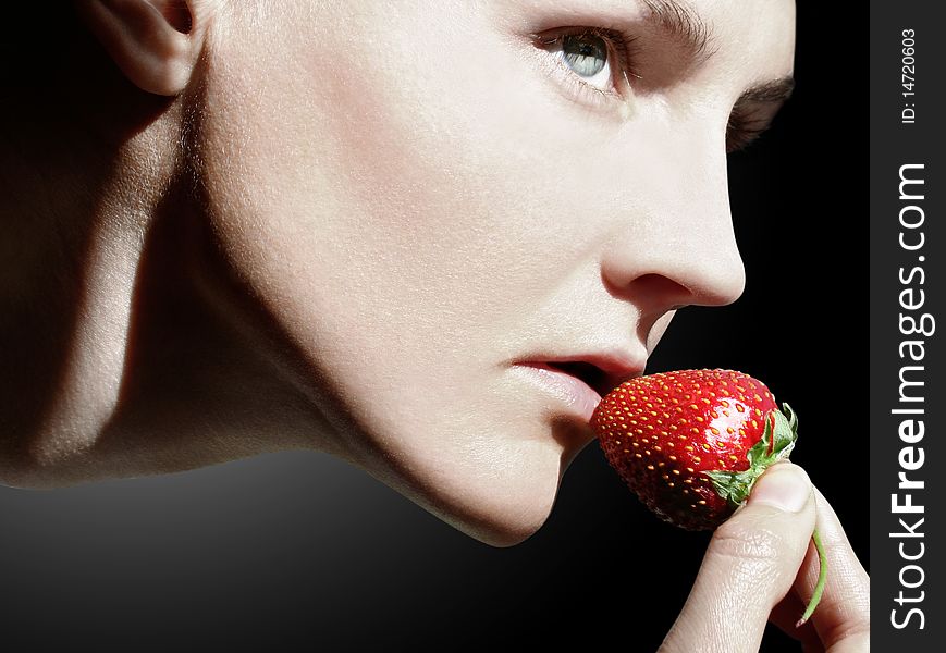 Young woman with a well-groomed skin brings to lips one strawberry. Young woman with a well-groomed skin brings to lips one strawberry