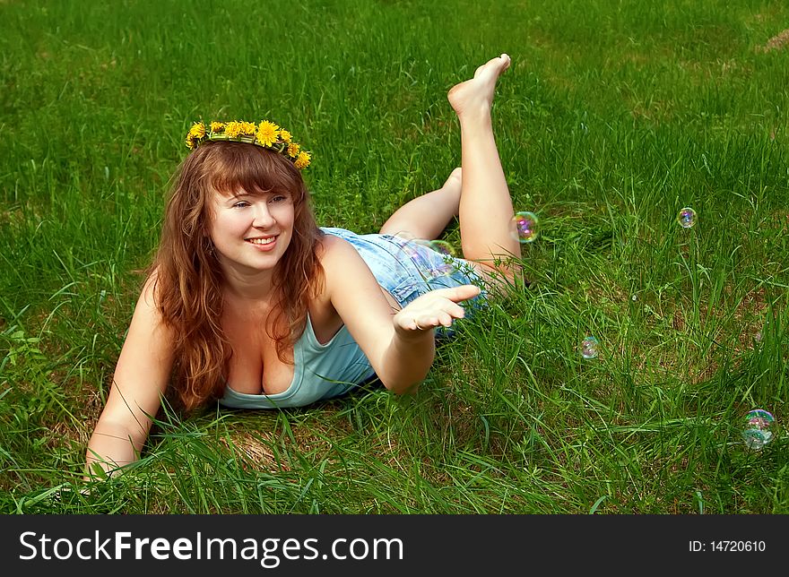 Portrait of a beautiful female with a dandelions garland, it is summer and she is playing with soap bubbles