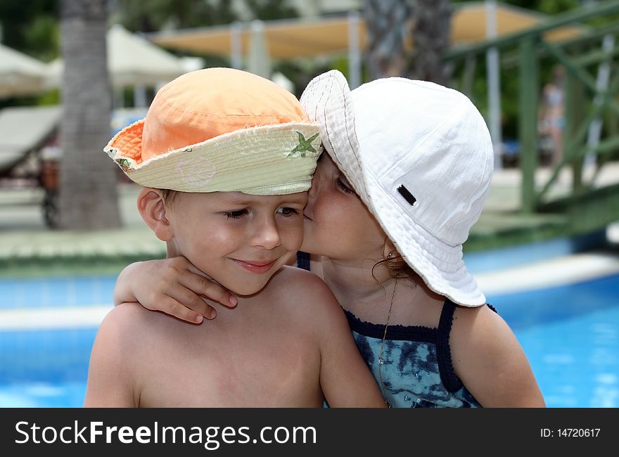 Little girl kissing a boy, on pool background