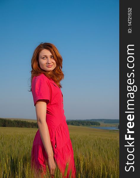 Redhead woman in red dress at wheat field sunset