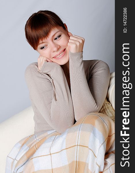 Young charming brunette in a gray jacket resting on the sofa