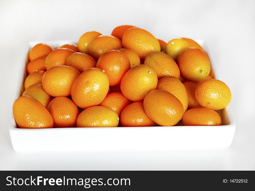 Kumquats piled on a white ceramic tray.