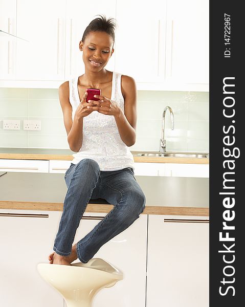 Woman Using Mobile Phone Sitting In Kitchen