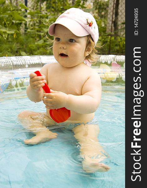 The surprised child with an open mouth in a cap with the big eyes sits in pool. The surprised child with an open mouth in a cap with the big eyes sits in pool