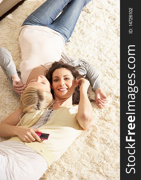 Two Women Listening To MP3 Player On Headphones Together Relaxing Laying On Rug At Home