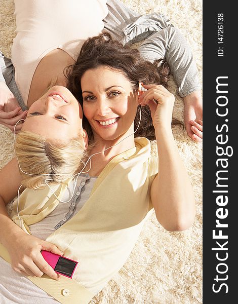 Two Women Listening To MP3 Player On Headphones Together Relaxing Laying On Rug At Home