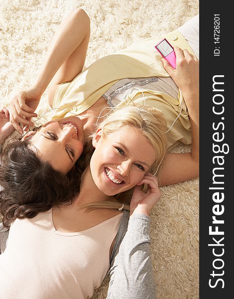 Two Women Listening To MP3 Player On Headphones Together Relaxing Laying On Rug At Home