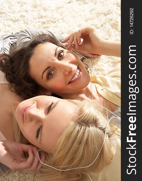 Two Women Listening To MP3 Player On Headphones Together Relaxing Laying On Rug At Home