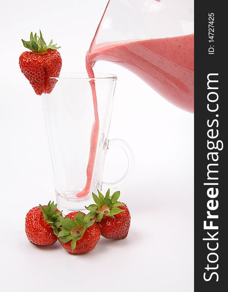 Strawberry shake being poured into a glass from a jug and some strawberries on white background