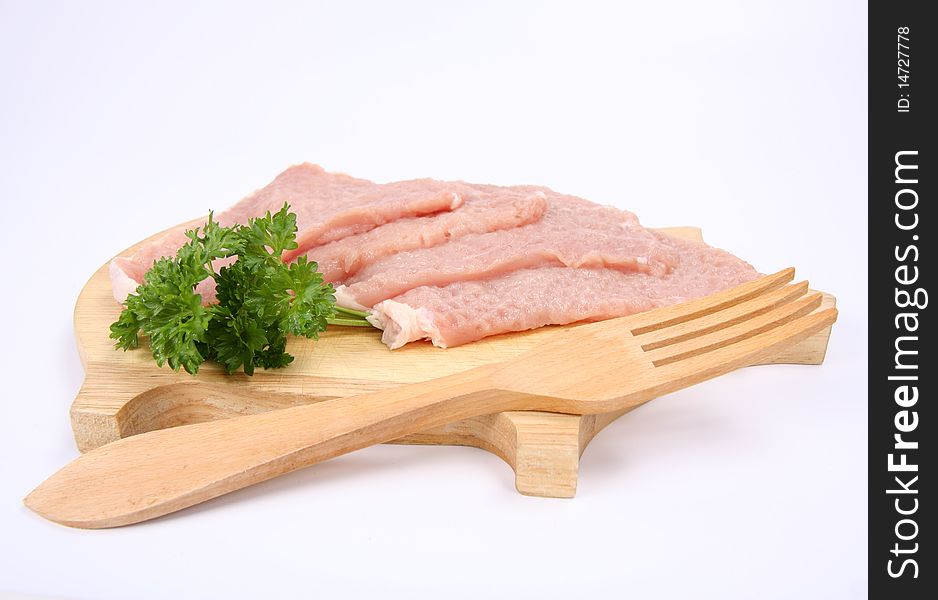 Raw tenderized pork chops on a pig shaped chopping board decorated with parsley and a wooden fork on white background