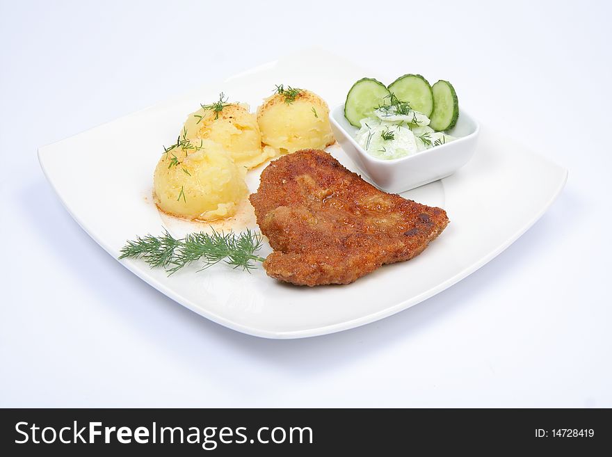 Pork chop (covered in batter and breadcrumbs), mashed potatoes and cucumber salad decorated with dill and parsley on a plate on white background. Pork chop (covered in batter and breadcrumbs), mashed potatoes and cucumber salad decorated with dill and parsley on a plate on white background