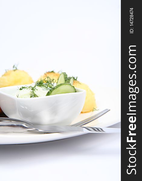 Cucumber salad in a bowl, with potatoes and a fork and a knife, on a plate, in close up