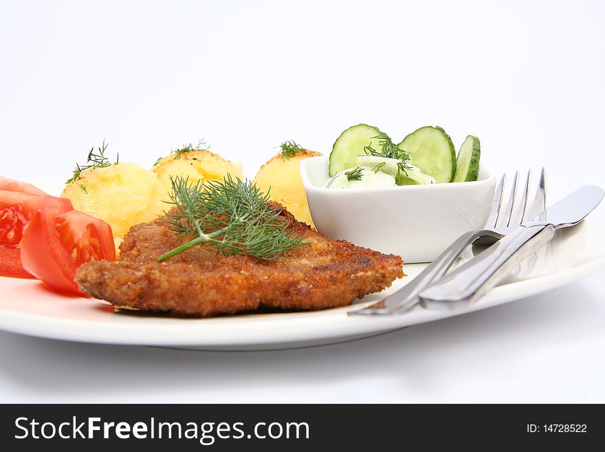 Pork chop (covered in batter and breadcrumbs), mashed potatoes and cucumber salad in a bowl decorated with dill on a plate with a fork and a knife on white background. Pork chop (covered in batter and breadcrumbs), mashed potatoes and cucumber salad in a bowl decorated with dill on a plate with a fork and a knife on white background