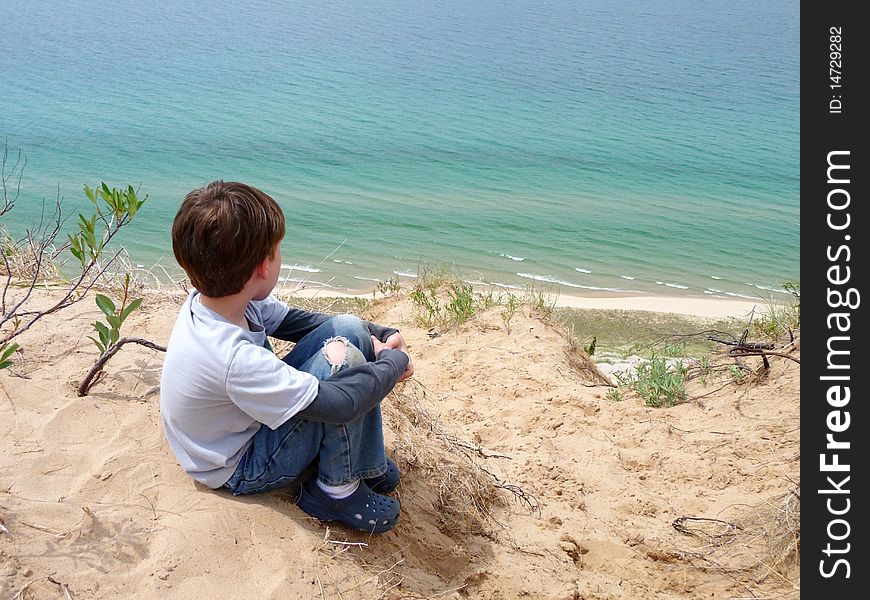 A young boy sitting atop a bluff looking down at Lake Michigan. A young boy sitting atop a bluff looking down at Lake Michigan.