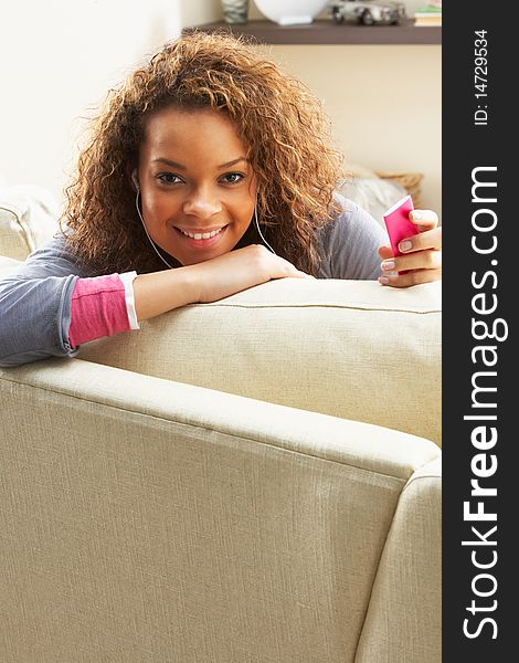 Woman Listening To MP3 Player On Headphones Relaxing Sitting On Rug At Home