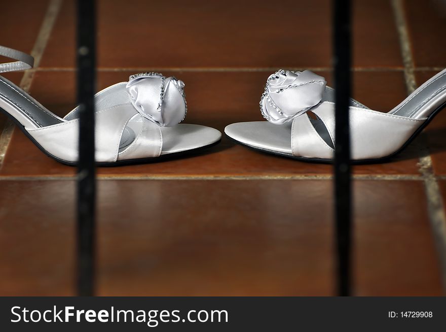 Wedding shoes inside bars on a red-tile floor