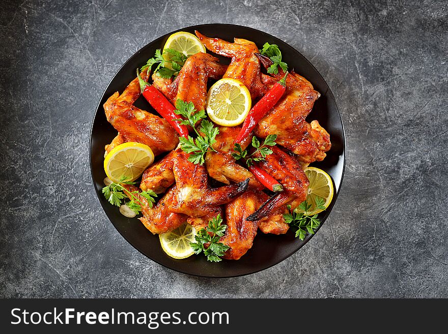 Delicious grilled chicken wings with lemon juice and chili pepper on gray concrete background. Top view. Copy cpace.