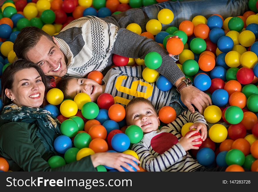 Happy family enjoying free time young parents and kids playing in the pool with colorful balls at childrens playroom