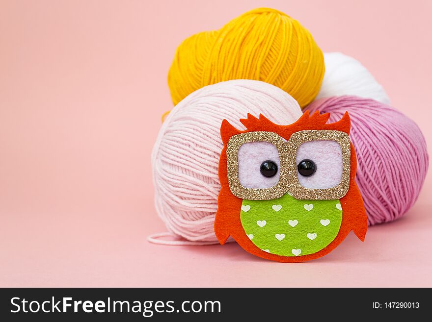 Self-made soft toy owl made of felt, on a color monophonic background. The owl stands next to the balls of yarn. There is a place