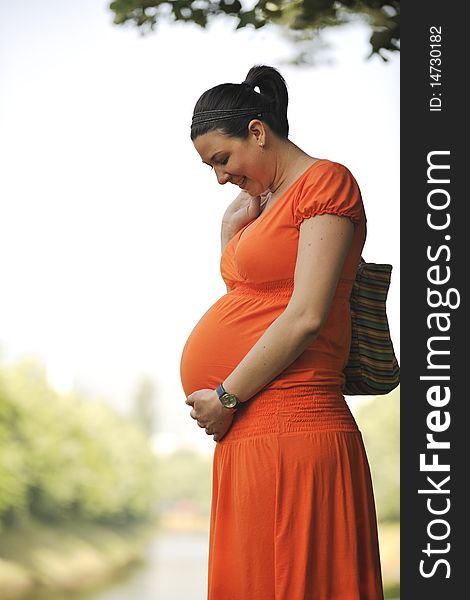 Beautiful young happy pregnant woman outdoor in bright nature in orange dress. Beautiful young happy pregnant woman outdoor in bright nature in orange dress