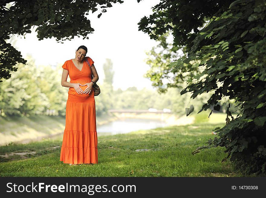 Beautiful young happy pregnant woman outdoor in bright nature in orange dress. Beautiful young happy pregnant woman outdoor in bright nature in orange dress