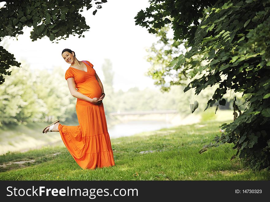 Beautiful young happy pregnant woman outdoor in bright nature in orange dress. Beautiful young happy pregnant woman outdoor in bright nature in orange dress